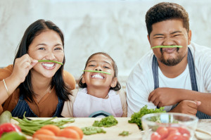 Asian, family and vegetables for playing in kitchen for portrait at table, happy or together. Mom, dad and child with smile in home at counter for health, food or nutrition in diet, dinner or cooking
